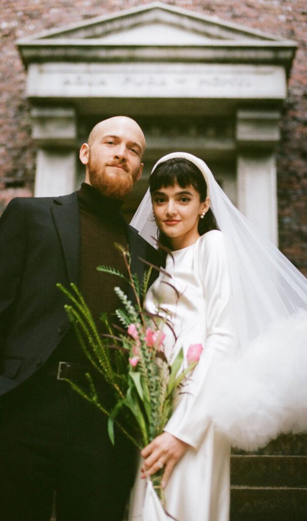 couple in front of classical stone building during courthouse elopement minimalist white dress black turtleneck blazer Seattle Washington
