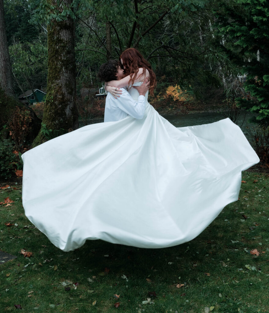 couple spinning during fall elopement in Washington State flowy white dress with autumn foliage and river in background