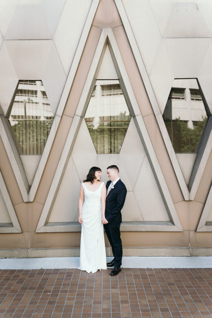 couple in city elopement outfits standing in front of geometric architecture Seattle Washington sleek white dress dark suit