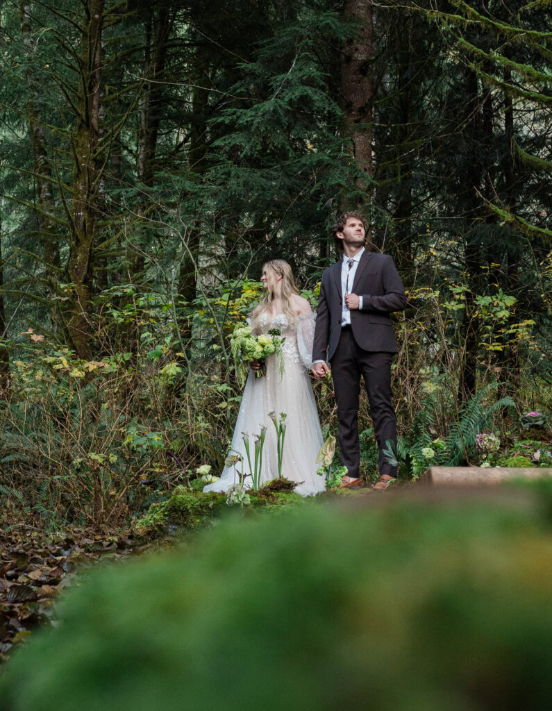 couple standing in lush Pacific Northwest forest during Washington elopement sparkly tulle dress dark suit green bouquet